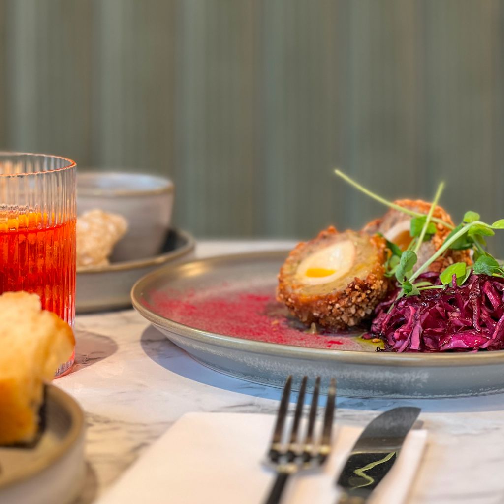 A crumbed Scotch egg cut in half, resting on a bed of red cabbage. 