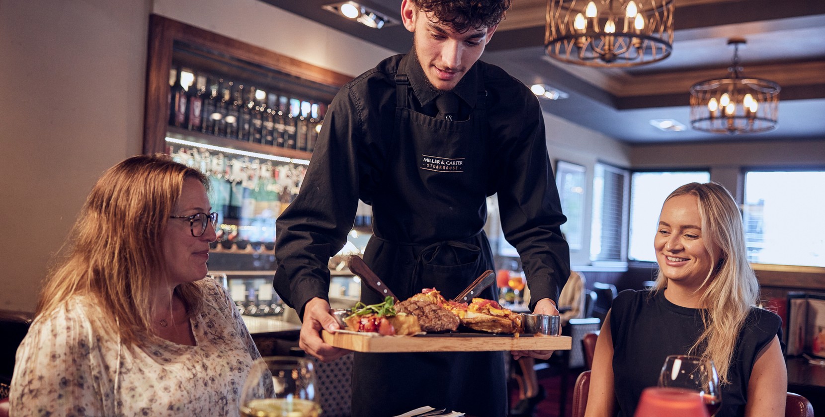 A team member at Miller &amp; Carter delivering a steak sharing board to guests. 