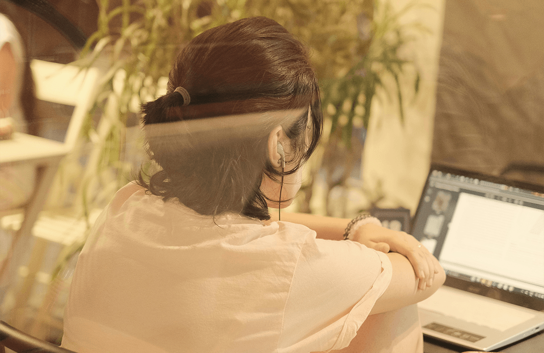 A person with their hair in a ponytail listening to a presentation on their laptop.