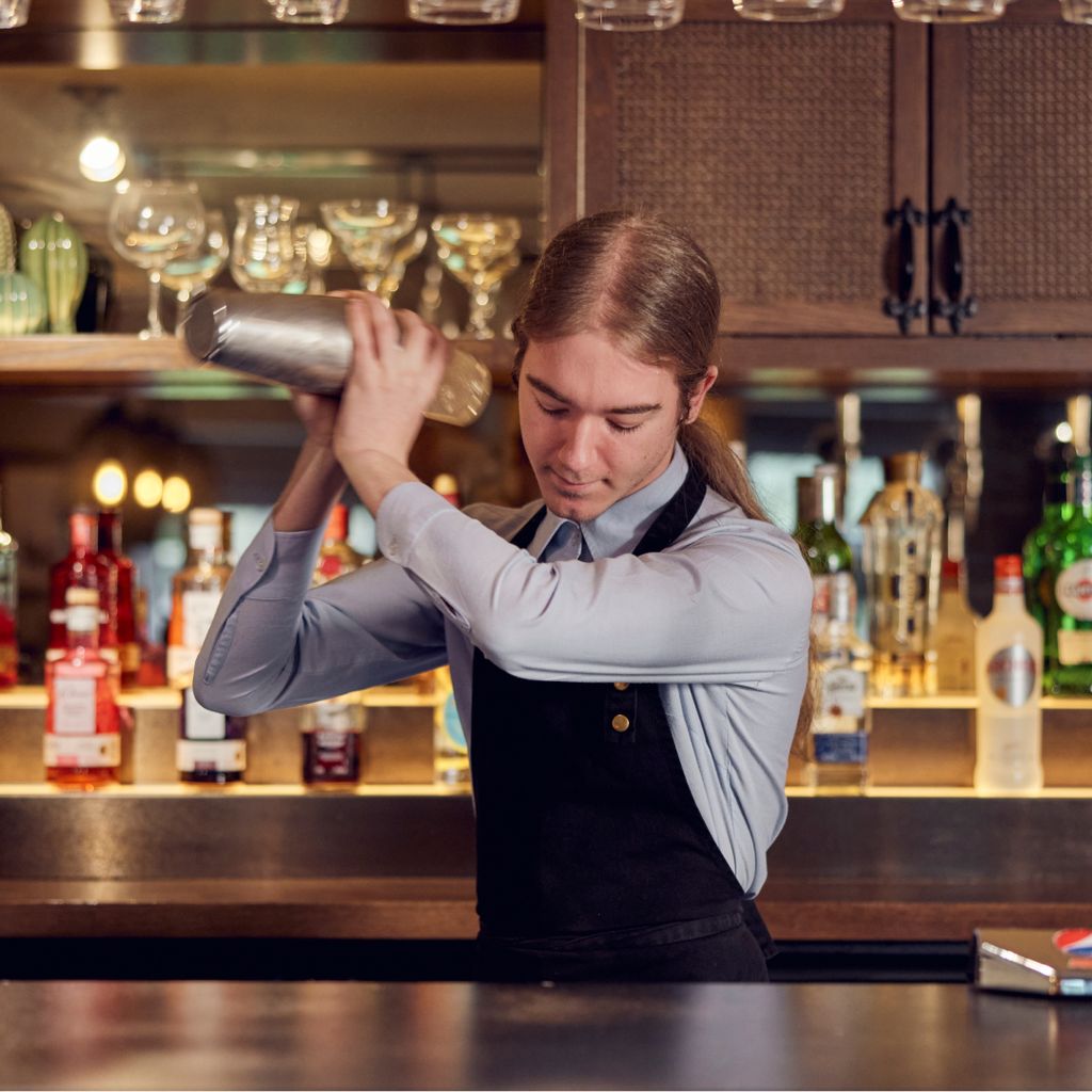 A bartender shaking up a cocktail behind the bar. 