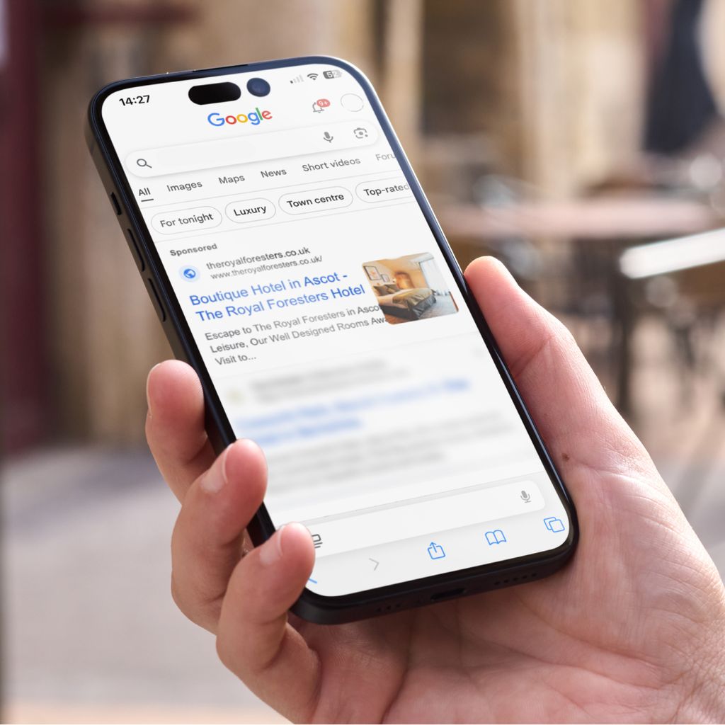 A hand holding an iPhone with an Oakman Inns hotel PPC ad showing.