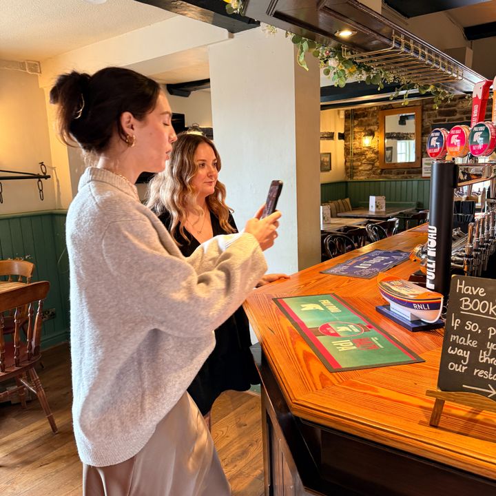 Beatrice taking footage with her phone at the bar of a Wadworth's pub.