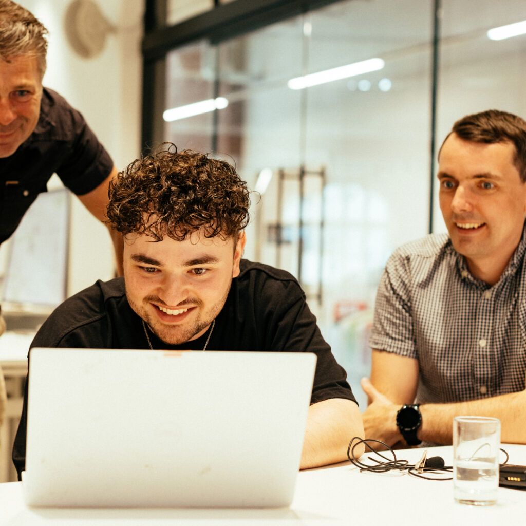 The team smiling while looking at a laptop screen.