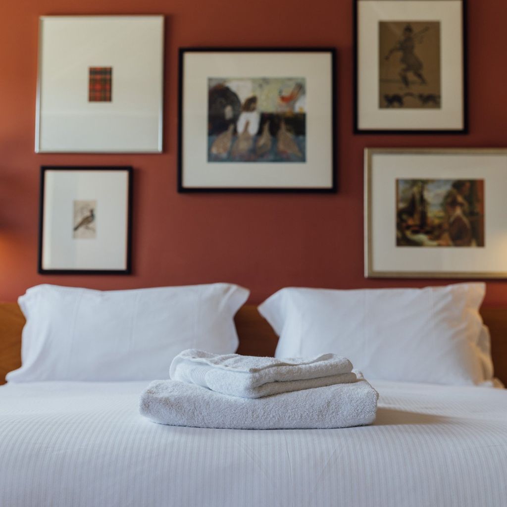 Towels folded on a made bed. In the background, an art-adorned wall.