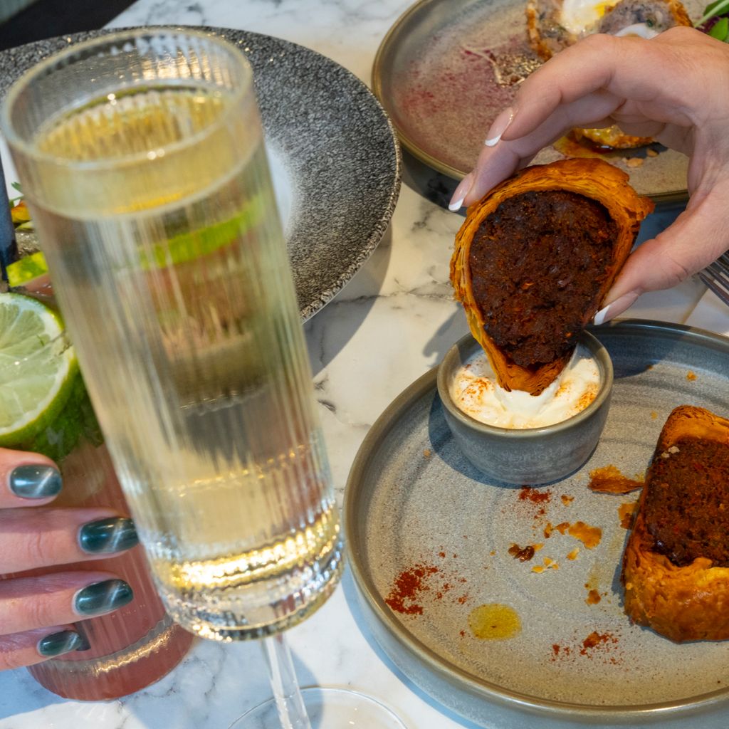 A meat-filled pastry being dunked into sauce. 