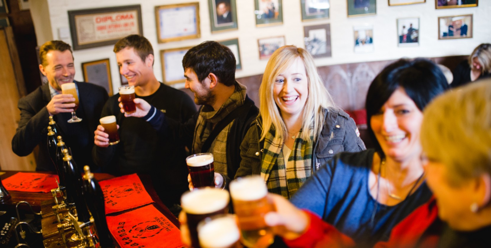 A group of people at the bar of a Batemans Pub, smiling and drinking pints. 