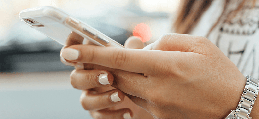 A young woman with painted nails typing on her iPhone.