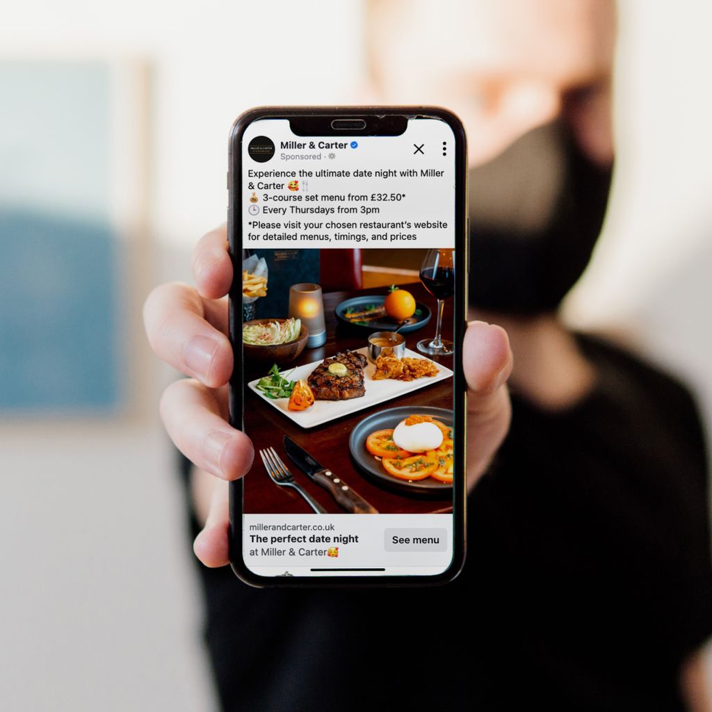 A man holds a phone towards the camera. On its screen, a Miller &amp; Carter social media post is displayed. 