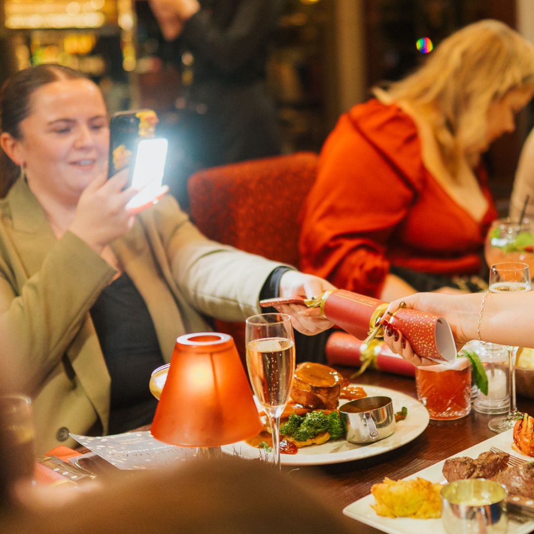 Social media content creators film themselves pull a Miller and Carter Christmas cracker over a festive dinner table.