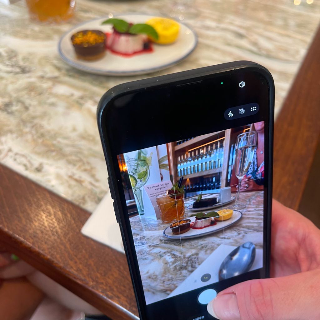 A person using a smartphone to photograph food and drink at a Pesto restaurant table.