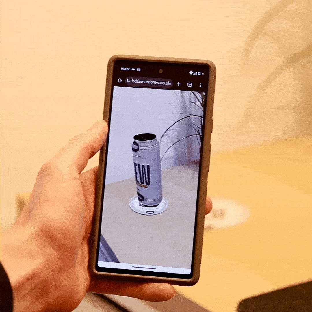 A Brew-branded AR beer mat. A beer can appears to be popping out on the phone’s screen. 