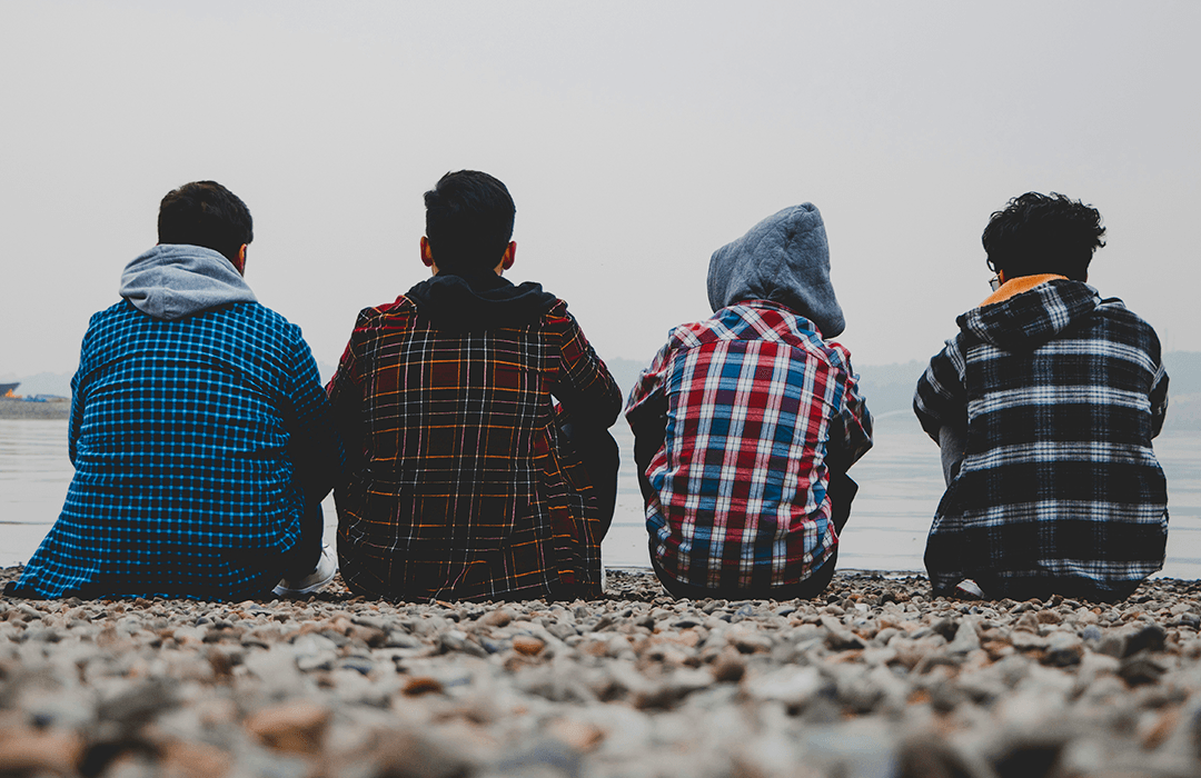Four teenagers sitting on the beach, looking out at the ocean.