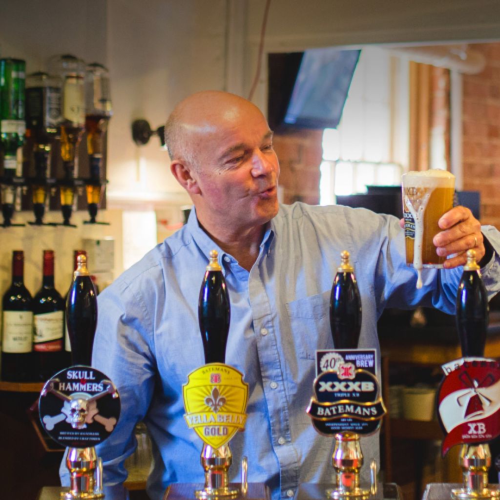 A man behind the bar of a pub, having just poured a fresh pint. 