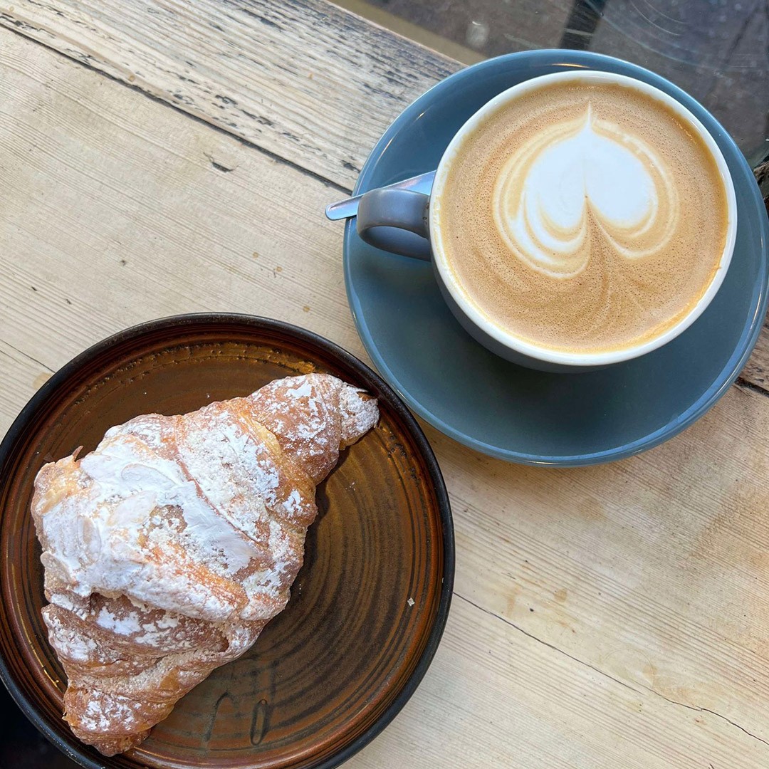 A foamy latte in a blue mug and a fresh, powder-dusted croissant.