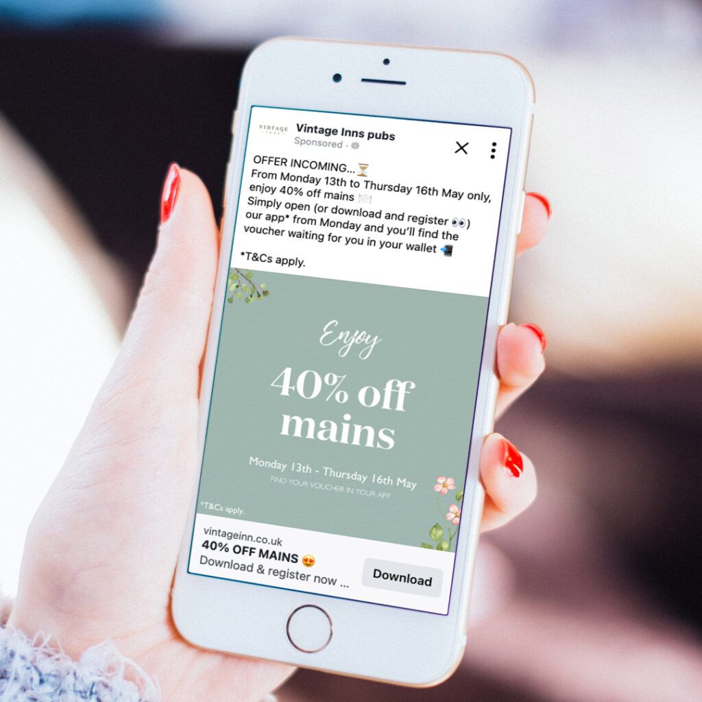 A person with red nails holding a phone. It displays a Vintage Inns social media post about 40% off mains. 