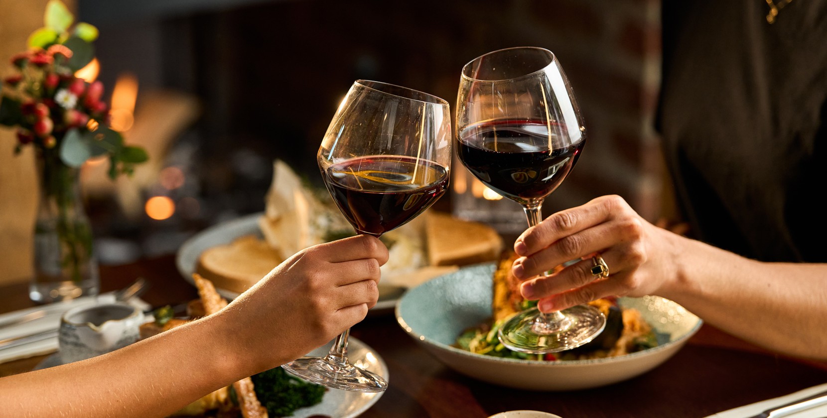 Two guests clinking their glasses of red wine while enjoying dinner. 